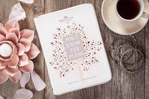 White devotional book with decorative cover on a wooden surface with flowers and a cup of coffee.