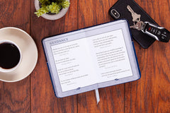 Open book displaying text about guidance for a graduate on a wooden table with a cup of coffee, keys, and a plant.