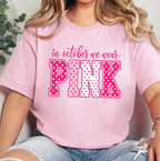 A woman wearing a light pink t-shirt with a graphic that reads 'in october we wear PINK' in pink and white polka dot lettering, paired with light-wash ripped jeans.