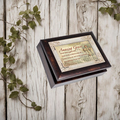 Dark burlwood music box with "Amazing Grace" lyrics and a silver cross on the lid, styled on a rustic white wood background with green vines.