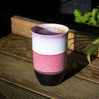 Multicolored ceramic mug on a wooden surface with plants in the background