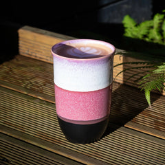 Multicolored ceramic mug on a wooden surface with plants in the background