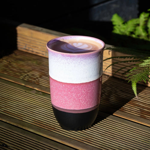 Multicolored ceramic mug on a wooden surface with plants in the background