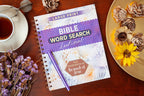 Bible Word Search devotional book on a wooden table with flowers and a cup of tea.