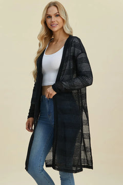 Woman wearing a black mesh cardigan over a white top and blue jeans on a beige background