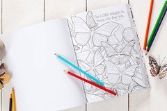 Coloring book with butterfly designs on a wooden surface with coloring pencils.