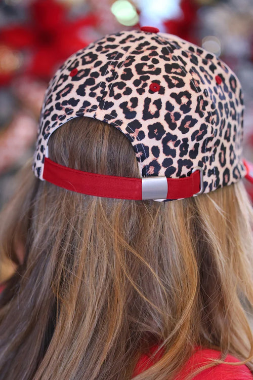 A close-up back view of a person wearing a leopard print baseball cap with a red adjustable strap and red button closure.