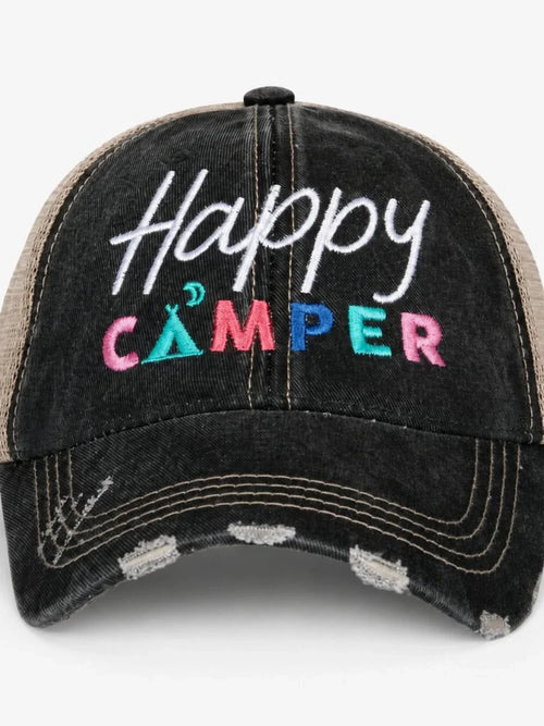 A distressed black trucker cap with 'Happy CAMPER' embroidered on the front. The front panel features a washed black denim-like texture with white, pink, blue, and green embroidery, while the mesh back is a natural tan/beige color.