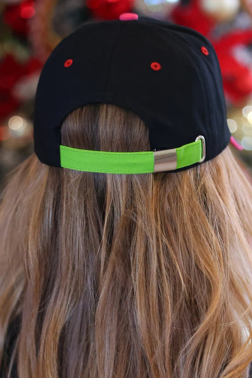 Back view of a person wearing a black baseball cap with a bright neon green adjustable strap and red eyelets, with long light brown hair visible.