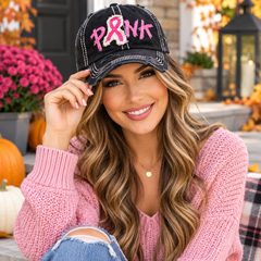 Woman wearing black distressed pink ribbon PINK baseball cap with pink sweater in an autumn setting