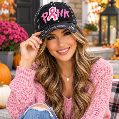 Woman wearing black distressed pink ribbon PINK baseball cap with pink sweater in an autumn setting