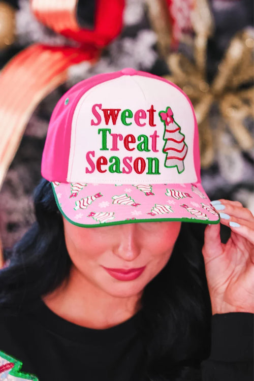 A woman wearing a pink and white trucker-style baseball cap with 'Sweet Treat Season' embroidered on the front and a pink brim covered in small candy cane prints.